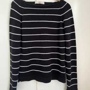 Svart och vit randig tröja från MARINE - Snygg svart tröja med vita ränder från MARINE. Tröjan har långa ärmar och en klassisk design som passar perfekt för både vardag och mer avslappnade tillfällen. Den är tillverkad i ett mjukt och bekvämt material.