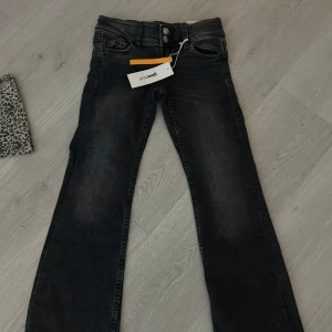 Svarta jeansbyxor med knappdetaljer - Snygga svarta jeansbyxor med klassisk femficksdesign och knappar bak. De har en rak passform och är perfekta för en avslappnad stil. Byxorna har en knapp och dragkedja framtill. Dem är i barnstorlek 134. Helt nya 