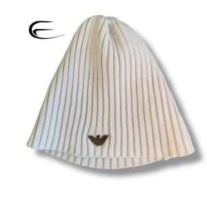 Vit ribbad mössa från Emporio Armani - Snygg vit ribbad mössa från Emporio Armani med det ikoniska logotypmärket framtill. Perfekt för att hålla värmen med stil under kyliga dagar.