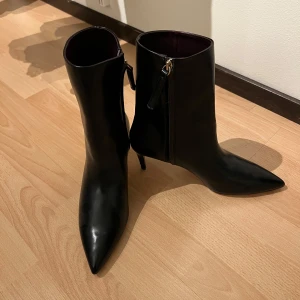 Svarta stövletter med spetsig tå - Eleganta svarta stövletter i skinn med spetsig tå och dragkedja på sidan. Perfekta för en stilren look.