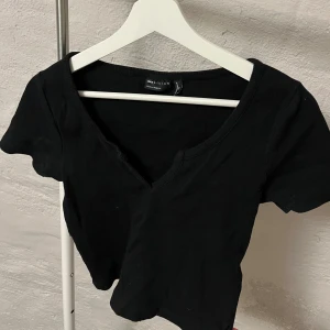 Kortärmad topp  - Säljer en stilren svart topp från ASOS Design. Den har en v-ringad hals och korta ärmar, perfekt för en enkel och snygg look. Tillverkad i ett mjukt material som ger en skön passform.