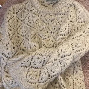 Beige stickad tröja med mönster - Mysig beige stickad tröja med ett vackert hålmönster. Perfekt för kyliga dagar med sin varma och bekväma design. Tröjan har långa ärmar och en rund halsringning. Superfin med jeans, säljer för att den tyvärr inte används längre men den har inga defekter alls !