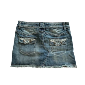 Jeanskjol med slitna detaljer - Snygg jeanskjol i en klassisk blå tvätt med slitna kanter och broderade detaljer på bakfickorna. Perfekt för en avslappnad och trendig look!