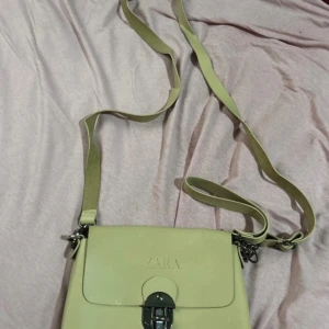 Beige axelväska från Zara - Snygg beige axelväska från Zara med justerbar axelrem och ett stilrent spänne framtill. Perfekt för att bära dina dagliga nödvändigheter med stil. Väskan har en enkel och elegant design som passar till många olika outfits.