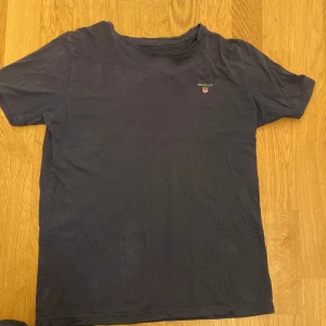 Svart t-shirt från GANT - Snygg svart t-shirt från GANT med korta ärmar och ett stilrent tryck av märkesloggan på bröstet. Perfekt för en avslappnad look.
