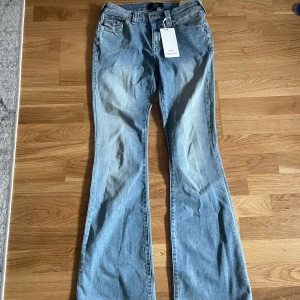 Blå bootcut jeans från True Religion - Snygga blå bootcut jeans från True Religion. De har en klassisk femficksdesign och en bekväm passform. Perfekta för en avslappnad stil med en touch av retro. Märkesetikett på baksidank och knappar i metall. Ny knappast använd