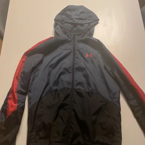 Svart och röd vindjacka från Under Armour - | Storlek S/M | 10/10 Skick | Nypris 1300kr | Mitt pris 750kr | Köpt av en vän (oanvänd) | Jackan är väldigt sällsynt | Priset är fast eftersom jackan är använd 2 ggr och är i topp skick | 