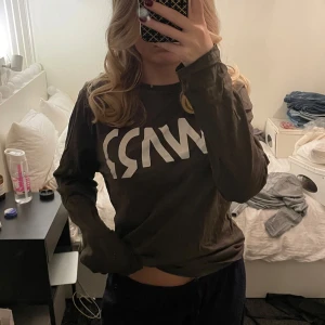 Olivgrön långärmad tröja från Warp - Säljer en olivgrön långärmad tröja från Warp med ett stort vitt tryck på framsidan. Perfekt att sova i eller träna i. Är lite blekt i halsen