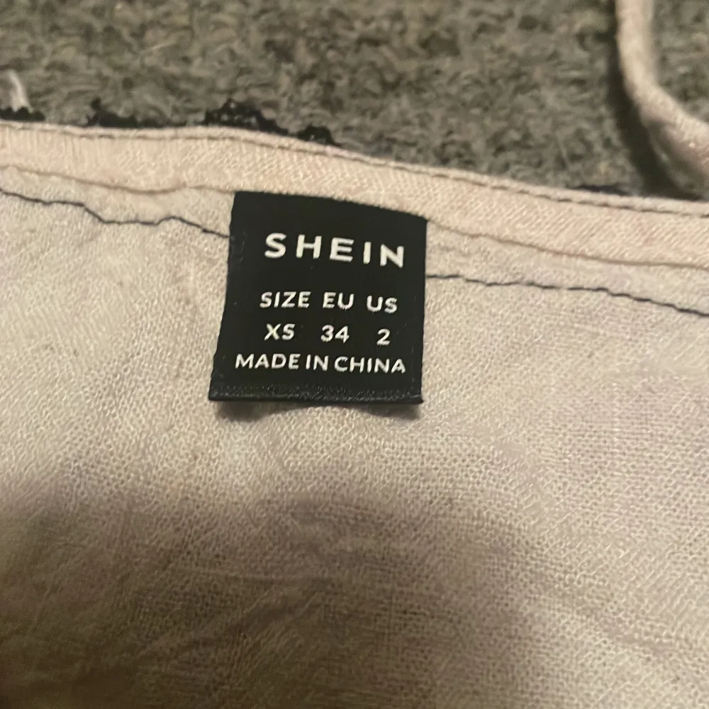 Säljer en söt beige topp från Shein med svarta spetsdetaljer vid axelbanden. Toppen är ärmlös och har en lätt croppad passform. Perfekt för varma dagar eller som ett lager under en jacka.. Yläosat.