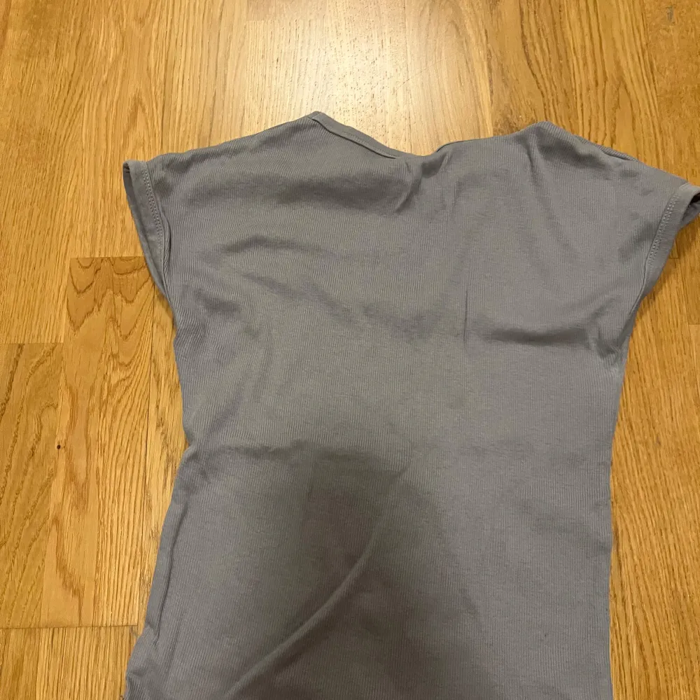 Säljer en stilren grå ribbad topp från Zara. Den har en enkel design med korta ärmar och rund halsringning. Perfekt för en avslappnad look.. Yläosat.