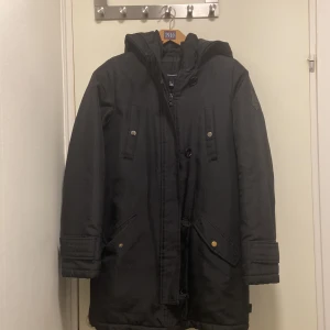 Svart parkajacka från Vero Moda - Snygg svart parkajacka från Vero Moda med huva och dragkedja. Jackan har knappar och praktiska fickor med tryckknappar. 