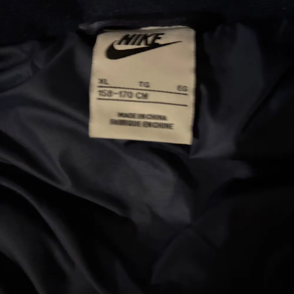 Säljer en svart dunväst från Nike med dragkedja framtill. Västen har en klassisk design med Nike-logga på bröstet och är perfekt för kyligare dagar. Den är lätt och bekväm att bära. Endbart testar den någon gång men gillade inte hur den satt på mig så den är i helt nyskick. Ganska stor i storleken skulle säga att den passar till 165-175 . Takit.