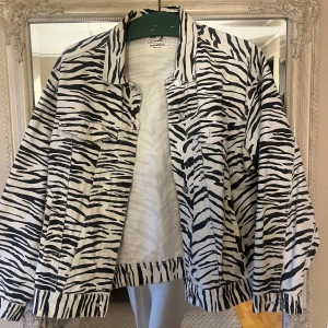 Zebramönstrad jeansjacka från Pull&Bear - Säljer en cool zebramönstrad jeansjacka från Pull&Bear. Jackan har en klassisk krage och knappar framtill. Perfekt för att ge din outfit en edgy touch 🖤