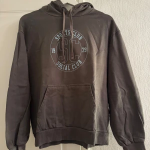 Grå hoodie med tryck från Cubus - Säljer en grå hoodie från Cubus med tryck på framsidan. Tröjan har en klassisk känguruficka och justerbar huva med dragsko. Perfekt för en avslappnad stil.