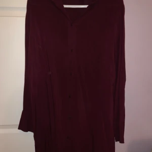 Vinröd skjorta från H&M - Snygg vinröd skjorta från H&M i storlek XL. Skjortan har långa ärmar och knappar framtill. Perfekt för en stilren look. Tröjan är ganska lång nertill