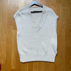 Beige stickad väst - Säljer en stilren beige stickad väst med v-ringad design. Västen har ribbade kanter och är perfekt för lager-på-lager-stil. Tillverkad av 92% akryl och 8% polyamid. Använd max 3 gånger.