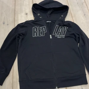 Svart hoodie från Replay storlek S,XS - Säljer en svart hoodie från Replay med dragkedja och tryck framtill. Den har en justerbar huva och långa ärmar. Perfekt för en avslappnad stil.