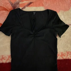 Svart ribbad topp från Bik Bok - Snygg svart ribbad topp från Bik Bok med korta ärmar och knytning framtill. Perfekt för en stilren look.
