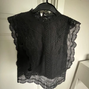 Svart spetsblus från ONLY - Säljer en elegant svart spetsblus från ONLY i storlek XS. Blusen har ett vackert spetsmönster och är ärmlös med fina detaljer runt hals och ärmslut.
