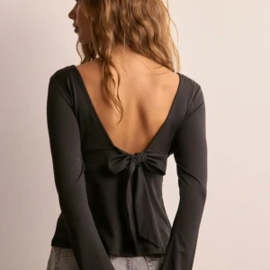 Svart långärmad topp med öppen rygg - Snygg svart långärmad topp med djup v-ringning och en elegant öppen rygg med knytning. Perfekt för en stilren look.