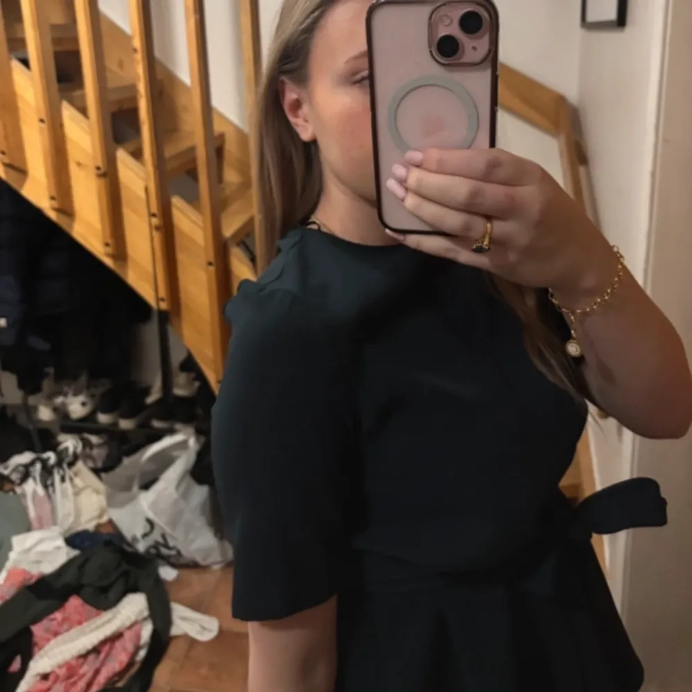 Snygg mörkgrön blus med knytband i midjan som ger en fin siluett. Blusen har korta ärmar och en rund halsringning. Perfekt för en stilren look.. Puserot.