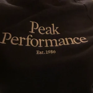 Mörk blå tröja från Peak Performance - Säljer en mörk blå tröja från Peak Performance med tryck 'Peak Performance Est. 1986' på framsidan. Tröjan har en klassisk design med ribbad krage och är perfekt för en stilren look.