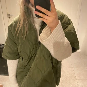 Grön quiltad jacka - Säljer en grön quiltad jacka med korta ärmar och dragkedja framtill. Jackan har en oversized passform och är perfekt för lager-på-lager-stil. Den är både trendig och bekväm, idealisk för kyligare dagar.