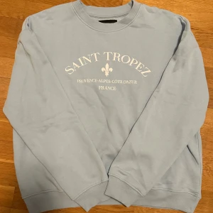 Ljusblå sweatshirt med Saint Tropez-tryck - Säljer en ljusblå sweatshirt med texten 'Saint Tropez' och 'Provence-Alpes-Côte d'Azur, France' tryckt på framsidan. Tröjan har långa ärmar och ribbade muddar vid ärmslut och nederkant. Perfekt för en avslappnad stil!💖✨