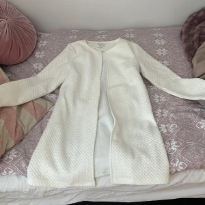 Vit kappa från VILA - Säljer en stilren vit kappa från VILA i storlek XS. Den har en elegant struktur och långa ärmar, perfekt för en chic look. Kappan är öppen framtill och har en mjuk känsla. Den är lång och passar till vår höst och sommar, aldrig använt förut 