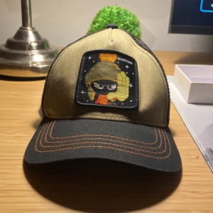 Beige och svart keps med broderad patch - Snygg keps från Capslab i grön och svart med en cool broderad patch framtill. Kepsen har ett nätmaterial baktill för extra ventilation och en justerbar rem för perfekt passform. Perfekt för en avslappnad stil.