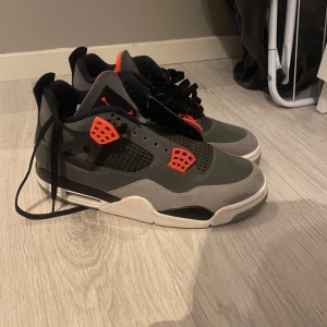 Nike Air Jordans 4 infrared  - Snygga Nike Air Jordans i en cool grå och orange färgkombination. Skorna har en klassisk design med snörning och en bekväm sula. Perfekta för dig som vill ha stil och komfort i ett.