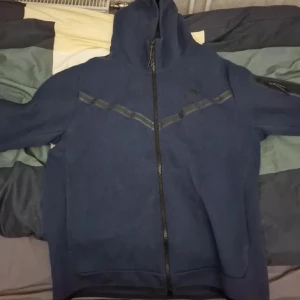 Blå mjukis sett från Nike - Säljer ett par bekväma blå mjukisbyxor och koftan från Nike med snörning i midjan och ribbade muddar vid bensluten. Perfekta för en avslappnad stil.