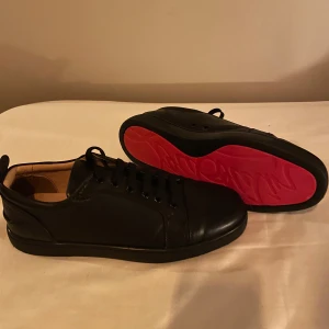 Loubs - svarta skor med röd sula  - Snygga svarta sneakers i skinn från Christian Louboutin med den ikoniska röda sulan. Skorna har snörning och en stilren design som passar perfekt för en trendig look. Priset är inte hugget i sten, pris kan diskuteras 