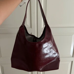 Vinröd väska - Snygg och rymlig väska i Burgundy. I skinnimitation, lite glansig. Kommer inte till använding längre 😊