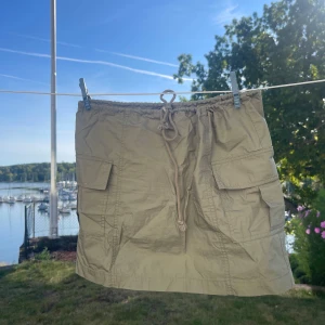 Beige kjol med fickor - Säljer en superfin grön kjol med stora fickor på sidorna. Den har en bekväm passform med knytband i midjan för justering. 