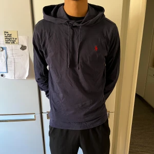 Mörkblå hoodie från Polo Ralph Lauren - Säljer en snygg mörkblå hoodie från Polo Ralph Lauren. Den har en klassisk design med en liten röd logga på bröstet och en bekväm huva med dragsko. Perfekt för en avslappnad stil och passar till alla tillfällen!