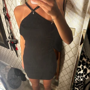Svart oneshoulder klänning - Säljer en snygg svart oneshoulder klänning som är perfekt för fest. Den är tight och kort, vilket ger en elegant och stilren look. Klänningen har en ribbad textur och en unik design med en axelbandslös stil på ena sidan.