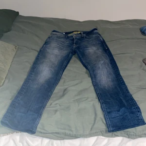 Blå jeans från Jack & Jones - Säljer ett par blå jeans från Jack & Jones i modellen Tapered Mike. De har en knappgylf och klassisk femficksdesign. Perfekta för en avslappnad stil. Jeansen är insydda vid benen så dem passa folk som är 160-165 cm 