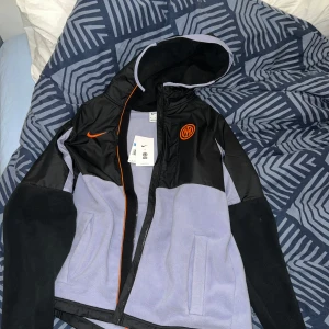 Nike jacka   - Säljer en Nike inter Milan vinterjacka(aldrig använd) Snygg svart och grå jacka från Nike med huva och dragkedja. Jackan har orangea detaljer och en logotyp på bröstet. Perfekt för sportiga aktiviteter eller som en stilren vardagsjacka. Mycket varm fleece i jackan (Limited edition jacka)