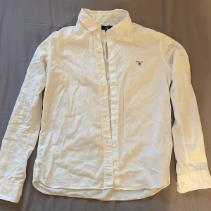 Vit skjorta från GANT - Säljer en klassisk vit skjorta från GANT som är i mycket bra skick och i storlek 170 cm. Perfekt för en stilren look.