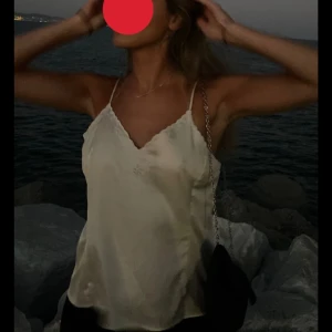 Beige sidenlinne festtopp med brodyr - Säljer ett elegant beige linne i siden med smala axelband och v-ringad hals. Perfekt för en sommarkväll vid havet. 