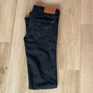Svarta low waist jeans  - Snygga svarta jeans från Replay med klassisk femficksdesign och knappgylf. Perfekta för en stilren look. Märkeslogga på bakfickan och läderpatch i midjan.