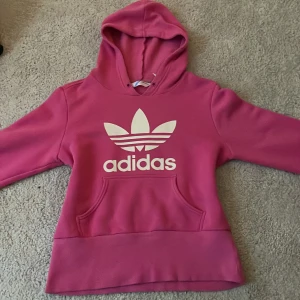 Rosa hoodie från Adidas - Jättesnygg och skön adidas hoodie med den gamla adidas loggan kvar och fin textur. Har bara använt tre gånger och är i helt nytt skick och jag säljer för att den tyvärr är för kort för mig💗. Den är assnygg till jeans men även snygg till sköna kläder💗💗💗