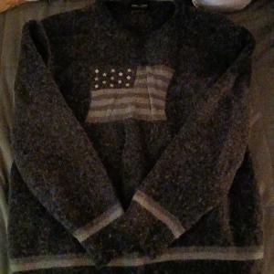 Grå tröja med flaggmönster - Säljer en mysig grå tröja, liknar Ralph Lauren, med ett stilrent flaggmönster på framsidan. Tröjan har långa ärmar och en bekväm passform, perfekt för kyligare dagar. Så snygg men har tyvärr aldrig använt, men Köpt secondhand❤️ På lappen står det 2XL men jag på bilden är xs/s så skulle säga att den passar mellan XS-L beroende på hur man vill att den ska sitta💕