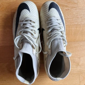 Nike fotbollsskor storlek 40,5 - Säljer ett par cremefärgade Nike fotbollsskor med svarta detaljer och snörning. Skorna har en strumpliknande passform och dobbar för bra grepp på planen. Perfekta för fotbollsträning och matcher. Använda en säsong. Några obehandlade fläckar annars topp! Kan hämtas vid Årstaberg i Stockholm.