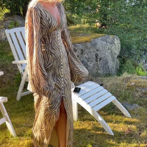 Zebramönstrad långklänning - Snygg zebramönstrad långklänning med knappar framtill och v-ringad hals. Klänningen har långa ärmar och en slits som ger en elegant touch. Perfekt för sommarens alla tillfällen.