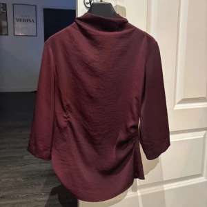 Vinröd blus med u-ringad rygg - Elegant vinröd blus med trekvartsärmar och en stilfull öppen rygg med knytband. Perfekt för en chic look.