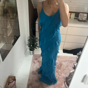 Blå långklänning med volanger - Snygg blå långklänning med volanger. Klänningen er aldrig brukt .Perfekt för en somrig look eller ball. Klänningen passar en s-m