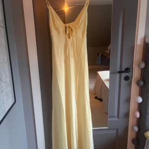 Gul satinklänning - Snygg gul långklänning med smala axelband och knytning framtill. Perfekt för sommarens varma dagar eller till balen. Klänningen är aldrig använd då jag hittat en annan. Lappen är kvar och den skickas i orginalförpackning💕