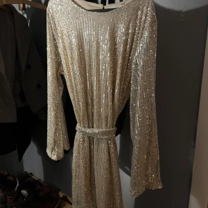Glittrig klänning från Rut & Circle - Säljer en glittrig klänning från Rut & Circle i storlek L. Klänningen har långa ärmar och ett bälte i midjan för en snygg passform. Perfekt för en festlig kväll!